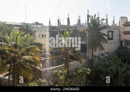 Hassan, Karnataka, Indien - 10. Januar 2023: Mit Blick auf eine Baustelle, die von mehreren Wohngebäuden und grünen Palmen umgeben ist Stockfoto