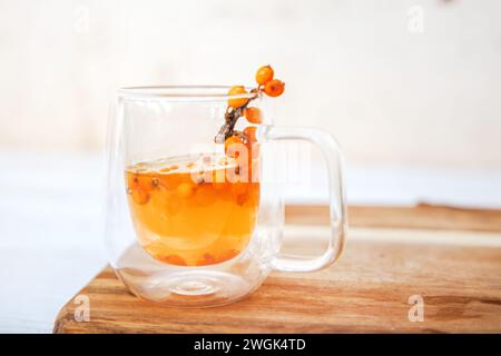 Tasse mit duftendem Vitamintee aus Sanddorn auf einem Holztisch. Frische Sanddornbeeren auf einem Zweig sind bereit für die Vorbereitung einer Heilung Stockfoto
