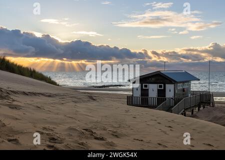 Die Küste von orth ist von ihrer schönsten Seite: Sonnenstrahlen, Dünen, Pier und Meer. Die untergehende Sonne verschwindet hinter einer dicken Schicht tief hängender Wolken. Stockfoto