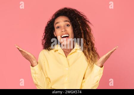 Überraschte schwarze Frau mit erhobenen Händen auf rosa Hintergrund Stockfoto