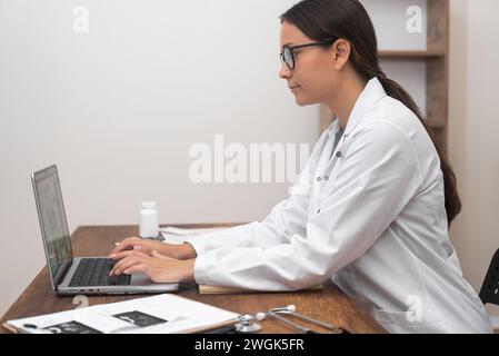 Ärztin, die sich auf Laptop konzentriert, leistet medizinische Unterstützung und führt Videokonsultationen durch Stockfoto