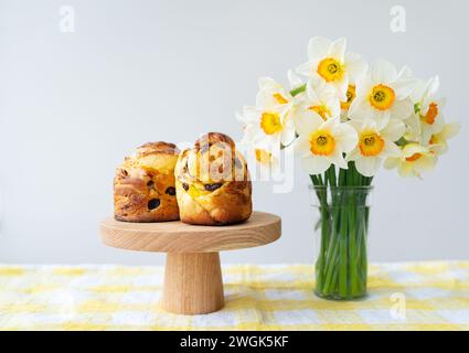 Frisches Gebäck auf einem Holzständer kombiniert mit einem hellen Duft von Narzissen auf einer karierten Tischdecke. Ostern Stockfoto