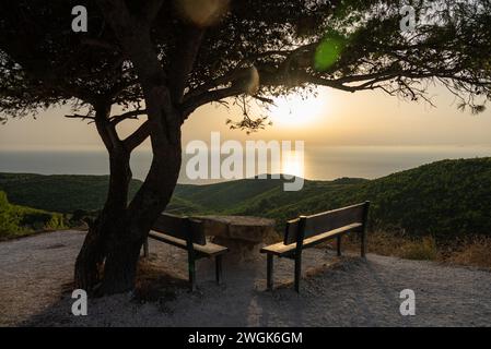 Pinien bei Sonnenuntergang, Olivenhaine und Meerblick. Bank mit Blick auf den Sonnenuntergang. Mediterraner Sonnenuntergang vom Aussichtspunkt Agalas. Sitzen und Sonnen beobachten Stockfoto