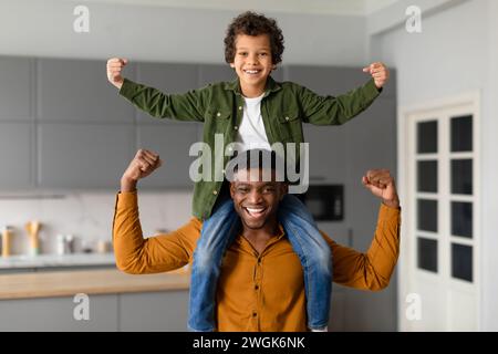 Fröhlicher schwarzer Vater und Sohn, der zu Hause die Muskeln zusammenspannt Stockfoto