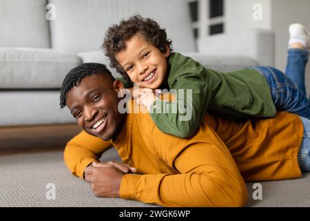 Schwarzer Vater und Sohn teilen sich einen spielerischen Moment auf dem Boden Stockfoto