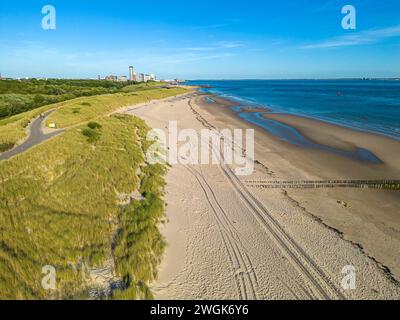 Aus der Vogelperspektive auf den Strand und die Stadt Vlissingen im Hintergrund, vor blauem Himmel. Stockfoto