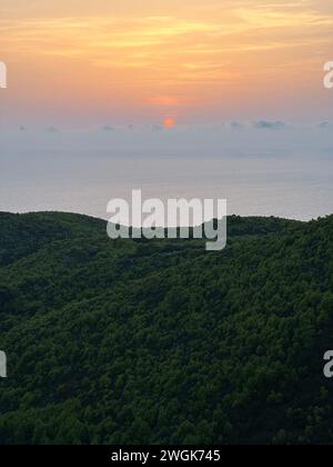 Pinien bei Sonnenuntergang, Olivenhaine und Meerblick auf einer griechischen Insel. Mediterraner Sonnenuntergang vom Aussichtspunkt Agalas. Sitzen und den Sonnenuntergang in Zakynth beobachten Stockfoto