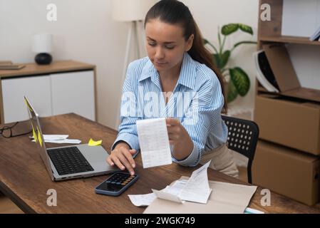 Die Frau berechnet Haushaltsausgaben auf dem Rechner, der zu Hause am Arbeitsplatz sitzt Stockfoto