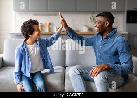 Fröhlicher schwarzer Vater und Sohn, der auf der Couch fröhlich ist Stockfoto