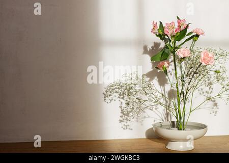 Wunderschöne rosa und weiße Blumen in der Schüssel auf rustikalem Hintergrund. Zarte florale Komposition auf Kenzan oder Blumennadel im Sonnenlicht. Moderne Blumengestalter Stockfoto