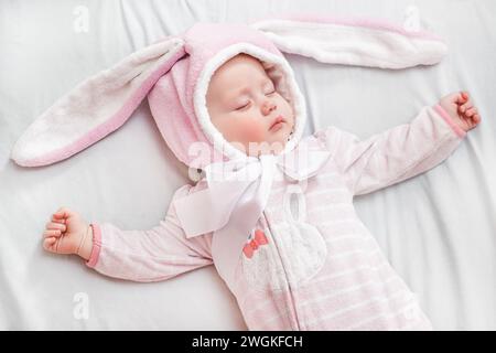 Das Neugeborene im Schlafanzug mit den Ohren eines Osterhasen liegt während eines Mittagsschlafens mit den Armen zur Seite. Stockfoto