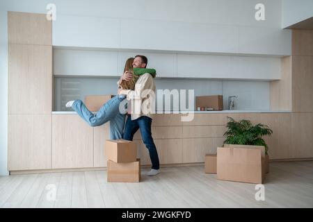 Glückliche, überglückte Frau und Mann umarmten sich in der Küche und zogen in eine neue Wohnung zwischen Pappkartons Stockfoto