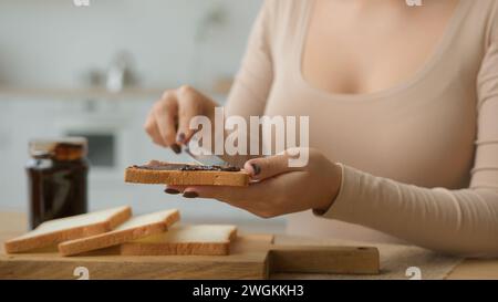 Cropped Shot weibliche Hände verteilen Schokoladenpaste Marmelade auf Toast Brot mit Messer kochen Morgen Frühstück bestellen Essen Lieferung aus Supermarkt unbekannt Stockfoto