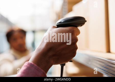 afroamerikanischer Lagerarbeiter hält Barcode-Scanner und führt Warenbestände durch. Mitarbeiter des Einzelhandelslagers scannen den Karton, um den Paketcode aus nächster Nähe zu überprüfen Stockfoto