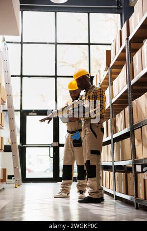 Lagerverwalter prüfen den Paketbestand anhand der Bestellcheckliste. Afrikanisch-amerikanischer Lagerleiter zeigt auf den Karton und erklärt das Vertriebsmanagement der Trainee Stockfoto