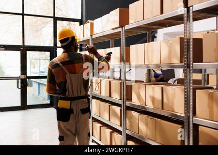 afroamerikanische Zustelldienstleiter scannen den Paketbarcode vor dem Versand. Alle Mitarbeiter der schwarzen Reederei verwenden Scanner auf Kartons im Lager Stockfoto