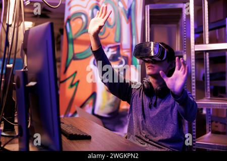 Junger Hacker, der vr-Technologie nutzt, um Server zu hacken und Passwort im Metaverse zu knacken. Mann, der ein Virtual-Reality-Headset trägt, während er in ein sicheres System einbricht, um vertrauliche Informationen zu stehlen Stockfoto