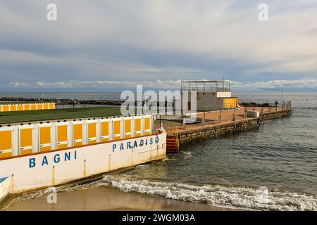 Erhöhter Blick auf den leeren Strand in der Nebensaison mit einer Reihe von Hütten und dem gemalten Schild des Badehauses 'Paradise Baths' im Winter, Sanremo, Ligurien Stockfoto