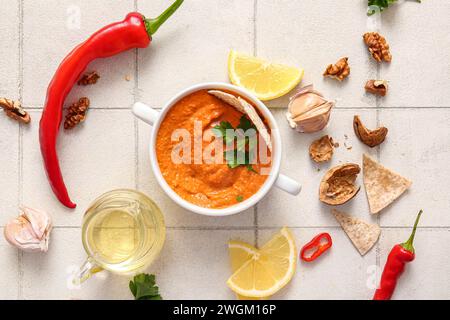 Topf mit leckerem Muhammara und Zutaten auf weißem Fliesenhintergrund Stockfoto