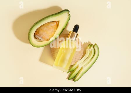 Frische Avocado mit Holzständer und Flasche ätherischen Öls auf beigefarbenem Hintergrund Stockfoto