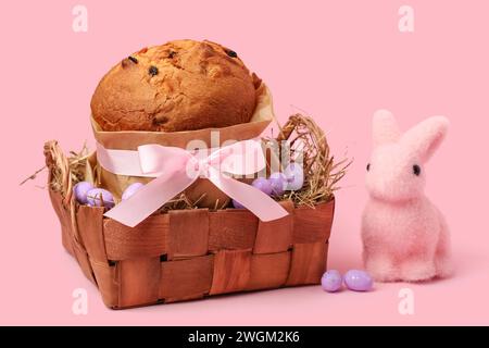 Korb mit köstlichem Osterkuchen, bemalten Eiern und Häschen auf rosa Hintergrund Stockfoto