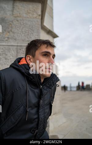 Junger braunhaariger Mann vorne auf der Straße, der auf jemanden mit müdem Gesicht wartet. Vertikal Stockfoto