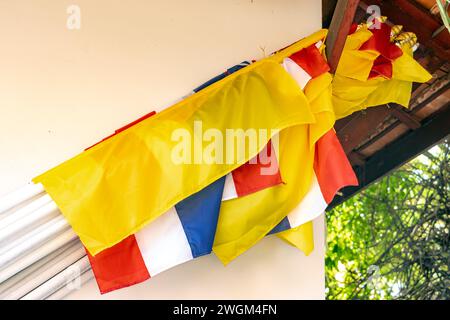 Eine Reihe von nationalen thailändischen Flaggen mit buddhistischer Flagge, die an die Wand eines Gebäudes in einem buddhistischen Tempel gelehnt sind Stockfoto