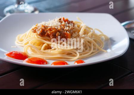 Spaghetti Bolognese mit Käse bestreut wird auf eine weiße Platte mit hölzernem Hintergrund gelegt Stockfoto