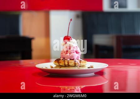 Mit Kirschen dekorierte Eispfannkuchen auf einem Teller auf einem roten Tisch Stockfoto