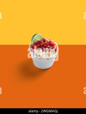 Maiszubereitung in einer Tasse, Esquite, mexikanischer Snack, Street Food, scharf, Chamoy, Chili Powder, minimalistischer orangener Hintergrund, keine Leute Stockfoto