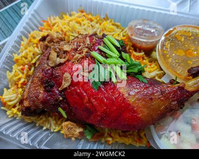 arabischer Reis mit roten Hähnchenschenkeln, farbenfroher Reis- und Currysuppe in einem weißen Plastikbehälter. Stockfoto