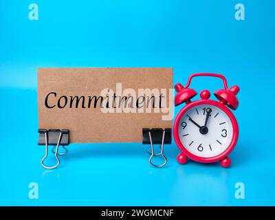 Roter Wecker und braune Karte mit Textverpflichtung auf blauem Hintergrund. Stockfoto