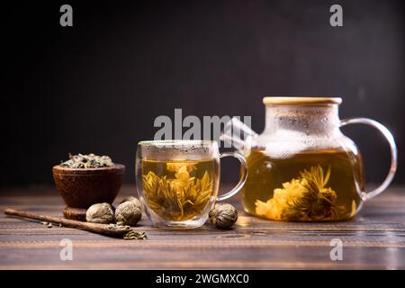 Teekanne und Glasbecher mit blühender Teeblüte auf einem Holztisch Stockfoto