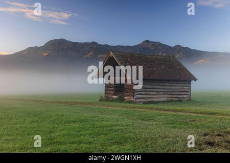 Alte Holzhütte bei Sonnenaufgang vor Bergen, Nebel, Sommer, Loisach-Kochelsee-Moor, Bayern, Deutschland, Europa Stockfoto