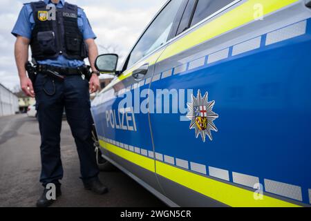 ILLUSTRATION - 31. Januar 2024, Saarland, Saarbrücken: Ein Polizeibeamter steht neben einem Streifenwagen, auf dem das Wappen der saarländischen Polizei zu sehen ist. Foto: Oliver Dietze/dpa Stockfoto