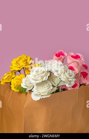 Schöner Rosenstrauß in einer Papiertüte auf rosa Hintergrund, Nahaufnahme Stockfoto