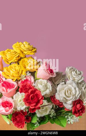 Ein Blumenstrauß aus bunten künstlichen Blumen in der Papierkarton auf rosa Hintergrund mit Kopierraum. Stockfoto