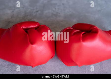 Ein Nahbild von roten Boxhandschuhen, die auf einer grauen Leinwandoberfläche liegen. Die Handschuhe sind nebeneinander angeordnet, wobei die Schnürsenkel zueinander zeigen. Stockfoto