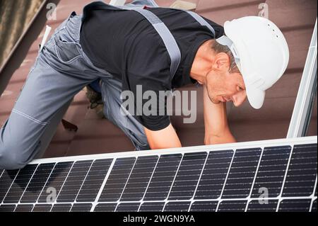 Mann Arbeiter, der Photovoltaik-Solarmodule auf dem Dach des Hauses montiert. Elektriker im Helm, der Sonnenkollektor im Freien installiert. Konzept alternativer und erneuerbarer Energien. Stockfoto