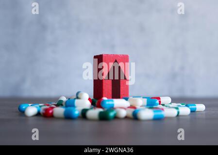 Ein roter Holzblock mit nach oben zeigendem Pfeil auf einem Haufen bunter Pillen. Steigende Kosten des verschreibungspflichtigen Medikamentenkonzepts. Stockfoto