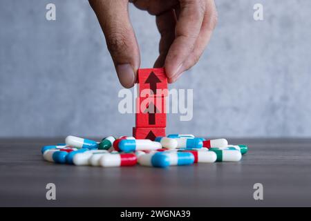 Ein roter Holzblock mit nach oben zeigendem Pfeil auf einem Haufen bunter Pillen. Steigende Kosten des verschreibungspflichtigen Medikamentenkonzepts. Stockfoto