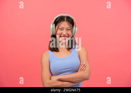 Junge lächelnde Chinesin isoliert auf rosafarbenem Hintergrund, Musik zu hören. Stockfoto