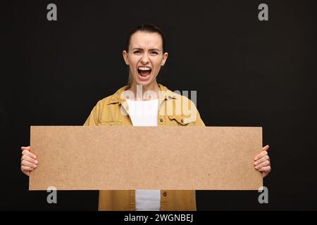 Schreiende Frau mit leerem Pappbanner auf schwarzem Hintergrund, Platz für Text Stockfoto