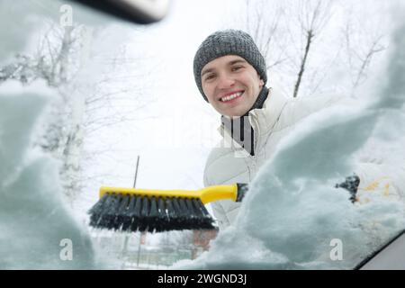 Mann, der Schnee von der Windschutzscheibe des Autos reinigt, Blick von innen Stockfoto