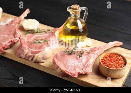 Frisches Tomahawk-Rindfleisch, Gewürze und Öl auf schwarzem Holztisch Stockfoto