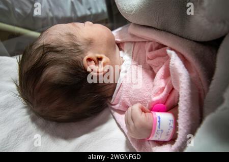 An ihrem ersten Lebenstag trägt ein neugeborenes Mädchen ein rosafarbenes Krankenhaus-ID-Armband an ihrer Hand Stockfoto