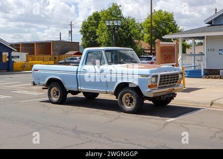 Ein klassischer blauer Pickup-Truck, der auf der Straße in einer kleinen Stadt mit umliegenden Gebäuden und klarem Himmel geparkt wurde. Stockfoto