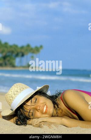 PUERTO RICO PORTO RICO junge hübsche Frau Porträt, die Sonne mit Strohhut Palmen und Strand Hintergrund am Meer nimmt Stockfoto