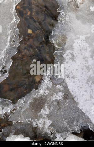 Ein schmaler kleiner Fluss im Winter, bedeckt mit Schnee und Eis, das Eis auf dem Fluss ist mit einem Kunststoff-geogitter verstärkt Stockfoto