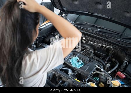 Asiatische Frau, die Probleme mit ihrem Auto hat schöne Frau, die kaputte Autos inspiziert, bevor sie zu Hause geht. Stockfoto